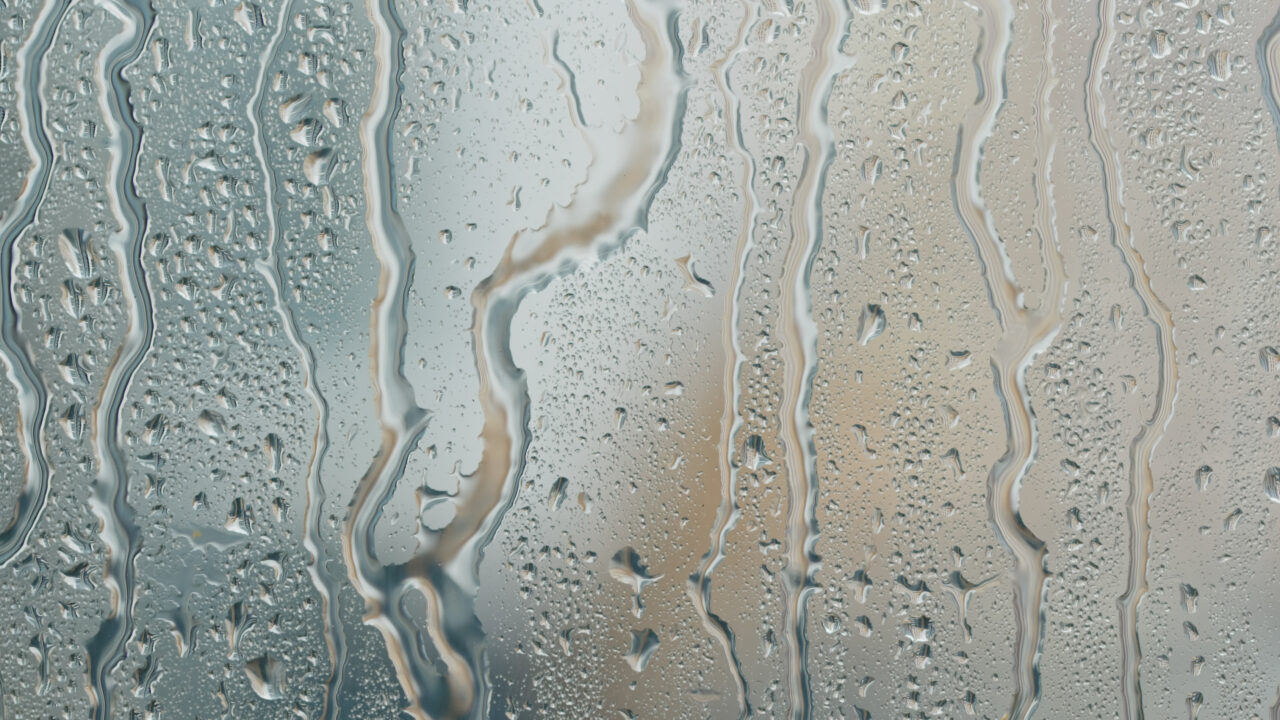 Close-up of water droplets on a glass window with blurred outdoor scenery, representing a rainy day and atmospheric mood.